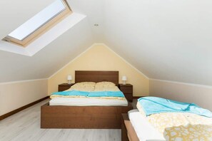 A bedroom with a sloped ceiling, a skylight, a bed with a wooden headboard, two bedside tables with lamps, and a bedside chair.