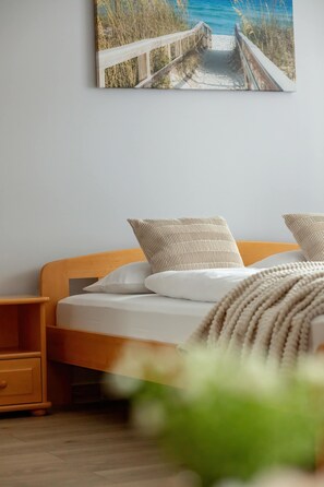Ein Schlafzimmer mit einem hölzernen Bett, weißer Bettwäsche, einem Nachttisch und einem Gemälde mit einer Strandansicht an der Wand.
