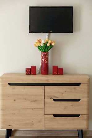 Eine hölzerne Kommode mit einem flachbildfernseher darüber, eine Vase mit gelben Tulpen und zwei rote Dekorboxen.
