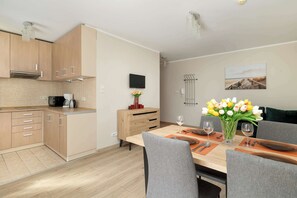 Eine moderne Küche mit Holzausstattung, einer Mikrowelle und einer Kaffeemaschine. Ein Esstisch ist gedeckt mit Tellern, Gläsern und einem Blumenstrauß.