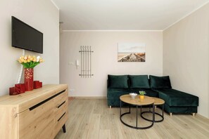 A modern living room with a wooden dresser, a green sofa, a round coffee table, and a flat-screen TV mounted on the wall.