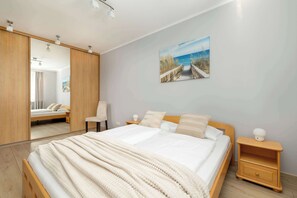 A bedroom with a large bed, a nightstand, a chair, and a painting of a beach scene.