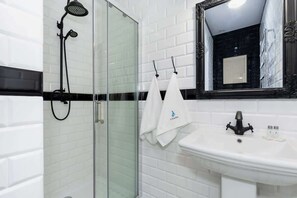 A modern bathroom with a glass-enclosed shower, a white sink with a black faucet, and a mirror with an ornate frame.