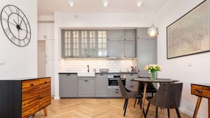 Una cocina moderna con armarios grises, piso de madera en patrón de espiga, un reloj negro y un comedor con dos sillas y una mesa.
