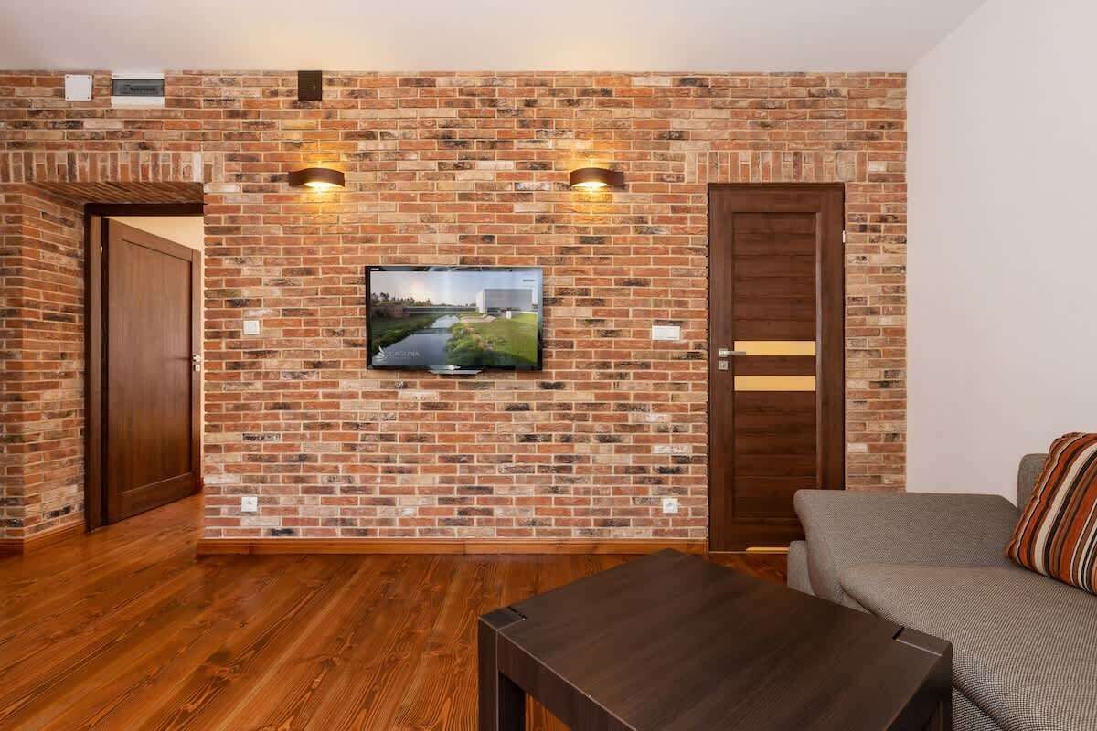 A living room with a brick wall, wooden floor, a television mounted on the wall, and a sofa.