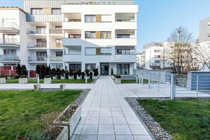 A modern multi-story residential building with balconies, a paved walkway, and landscaped areas.