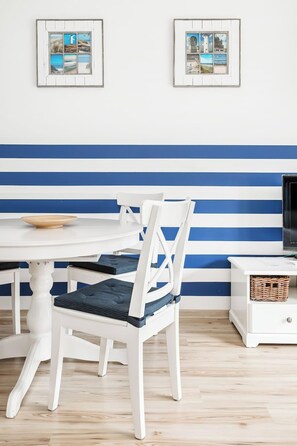 A dining area with a white table and chairs, a blue-striped wall, and two framed pictures above the table.