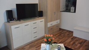 Una sala de estar moderna con un televisor de pantalla plana, parlantes y un mueble. Hay una mesita con un florero y una vela.