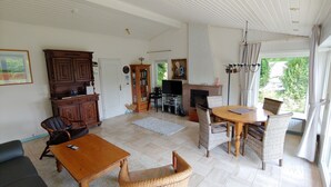 A spacious living room with a fireplace, a television, and a dining area with wicker furniture. - Beautiful detached holiday home with a sunny location and panoramic views (Lissendorf)