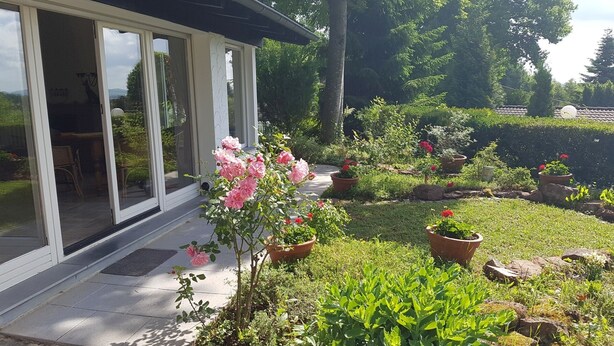 A garden with potted plants and a patio area with a glass door leading to a room. - Beautiful detached holiday home with a sunny location and panoramic views (Lissendorf)