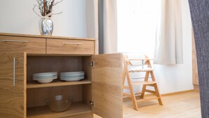 Een houten kast met open planken, waarin borden, kommen, een ladder en een vaas met takken staan.