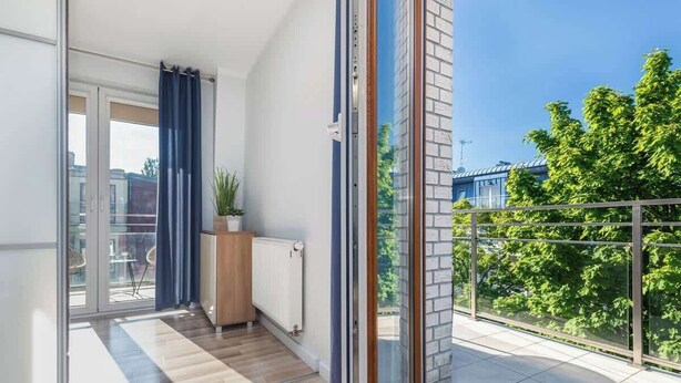 A balcony with a view of trees and buildings, a sliding glass door, and a radiator.