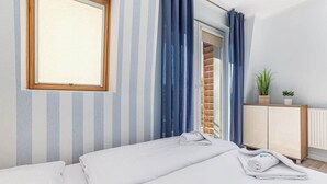 A hotel room with a bed, a window, a radiator, and a plant.