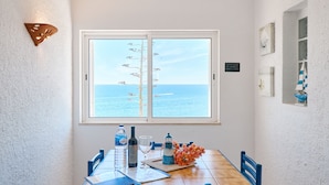 Un coin repas avec vue sur la mer, une bouteille d’eau, une bouteille de vin et une petite maquette de phare posés sur la table.