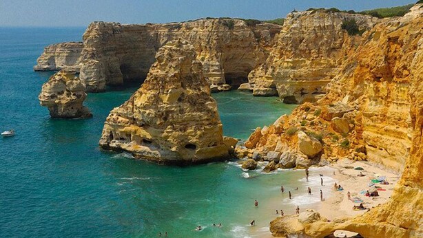 Une plage côtière bordée de falaises rocheuses et baignée d’eaux turquoise et cristallines.
