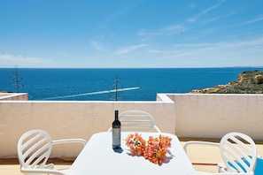 A table with a bottle and flowers on a balcony overlooking the sea.