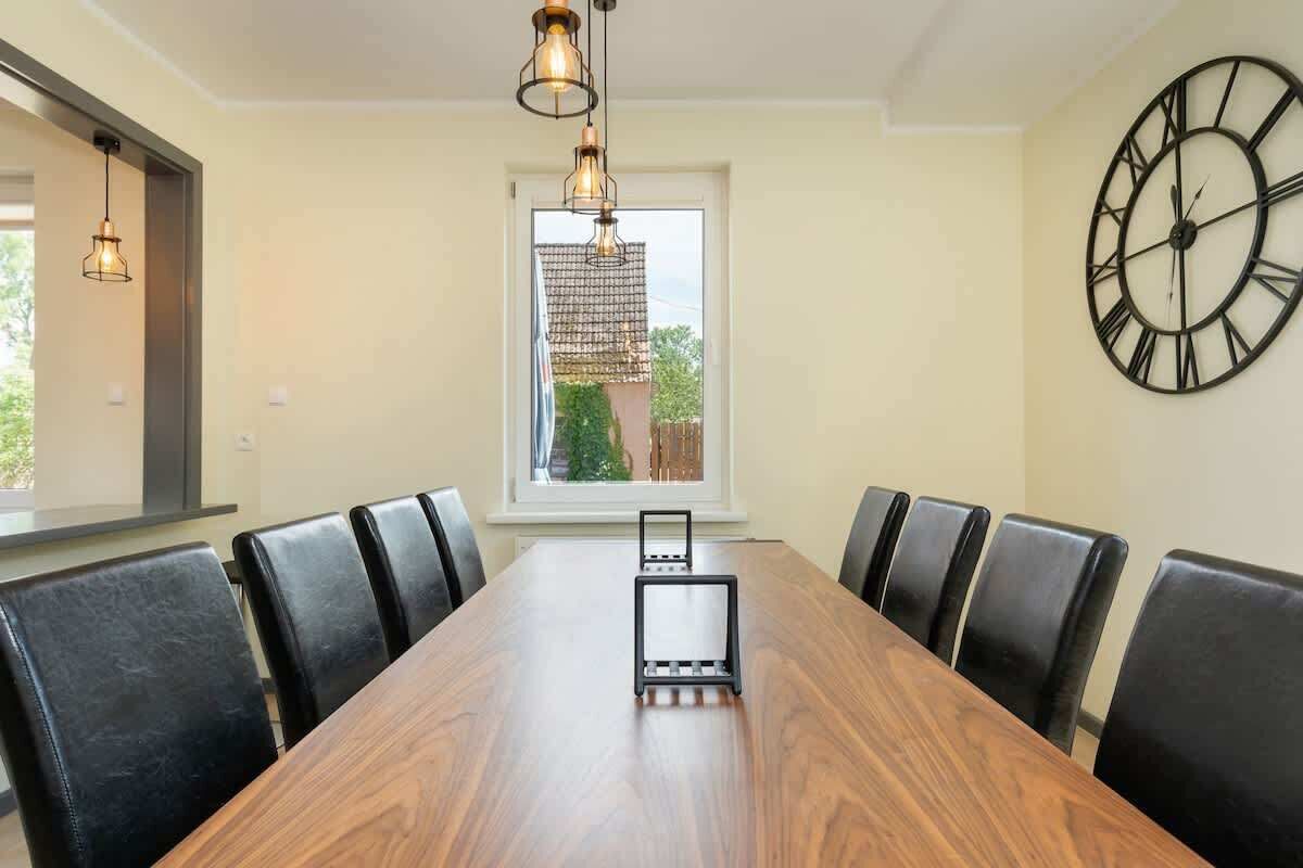 A conference room with a wooden table, black chairs, a large wall clock, and hanging pendant lights.