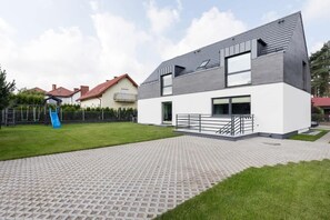 Una casa moderna de dos pisos con techo plano, ventanas amplias y entrada pavimentada.