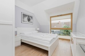 A modern bedroom with a bed, bedside tables, a window with a view, and a framed picture on the wall.