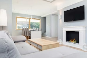 Una sala de estar moderna con chimenea, televisor de pantalla plana y comedor con vistas al exterior.