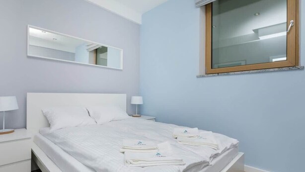 Un dormitorio con una cama, mesitas de noche blancas, un espejo y una ventana.