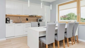 Una cocina moderna con armarios blancos, una isla central y una zona de comedor con sillas grises.