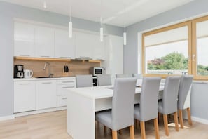 Una cocina moderna con armarios blancos, una isla central y una zona de comedor con sillas grises.