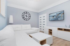Un salón moderno con un sofá blanco, una mesa de centro, un televisor y un reloj de pared.