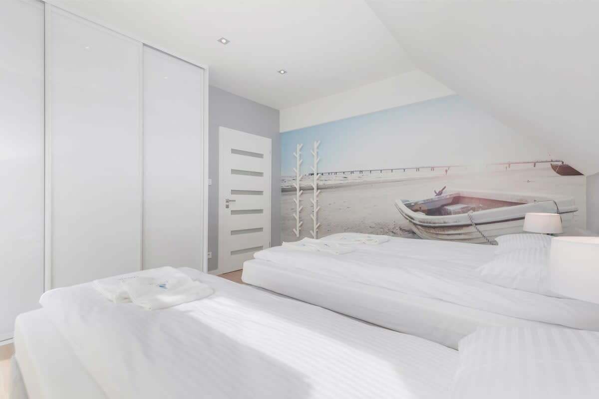 Ein Schlafzimmer mit zwei Betten, einem weißen Kleiderschrank und einem Wandgemälde mit einer Strandansicht.