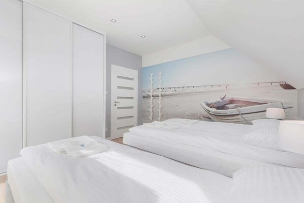 Ein Schlafzimmer mit zwei Betten, einem weißen Kleiderschrank und einem Wandgemälde mit einer Strandansicht.