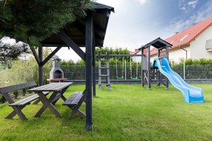 Un parque infantil con tobogán y columpios, una mesa de picnic y una parrilla.