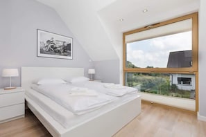Un dormitorio moderno con una cama grande, dos mesitas de noche, un cuadro enmarcado en la pared y un ventanal con vistas al exterior.