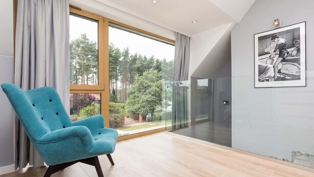 Una habitación moderna con un ventanal grande, un sillón azul y un cuadro en la pared.