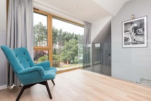 Una habitación moderna con un ventanal grande, un sillón azul y un cuadro en la pared.