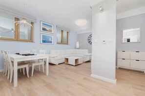 Ein modernes Wohnzimmer mit einem weißen Sofa, einem Esstisch mit Stühlen und einer Küchenzeile mit Schränken.