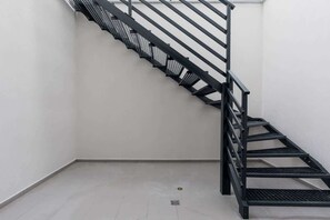 Eine schwarze Metalltreppe in einer Ecke eines Raumes mit weißen Wänden und einem gefliesten Boden.