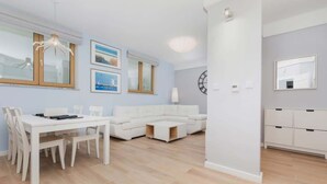 A modern living room with a white sofa, a dining table with chairs, and a kitchen area with cabinets.