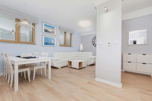 Una sala moderna con un sofá blanco, una mesa de comedor con sillas y una zona de cocina con armarios.