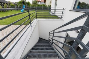 Eine moderne Treppe mit Metallgeländern führt zu einer Dachterrasse mit grüner Rasenfläche und einem Spielplatz.
