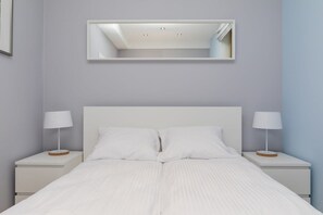 Ein modernes Schlafzimmer mit einem weißen Bett, zwei Nachttischen, einem Spiegel und einer Deckenleuchte.