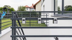 A modern building with a balcony, a fenced play area with a slide, and a house in the background.