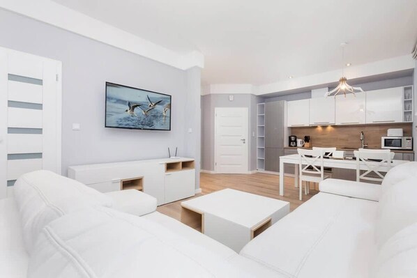 Una sala de estar moderna con sofás blancos, un comedor y una cocina con armarios blancos y una encimera de madera.