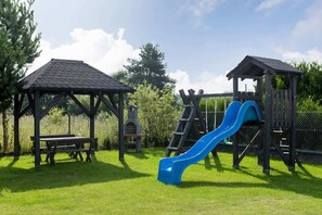 Un parque infantil con un tobogán, una mesa de picnic y dos refugios de madera.