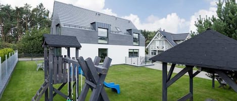 A modern house with a large deck, a slide, and a gazebo.
