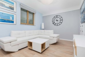 Una sala de estar moderna con un sofá seccional blanco, una mesa de centro de madera y un reloj de pared grande.