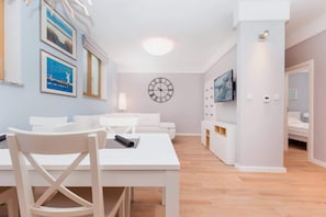 A modern living room with a white sofa, a dining table with chairs, and a wall clock.