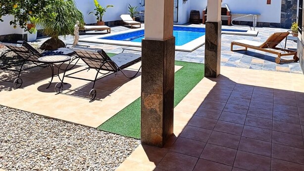 Un espacio al aire libre techado con piscina, sillas de descanso y una parrilla.