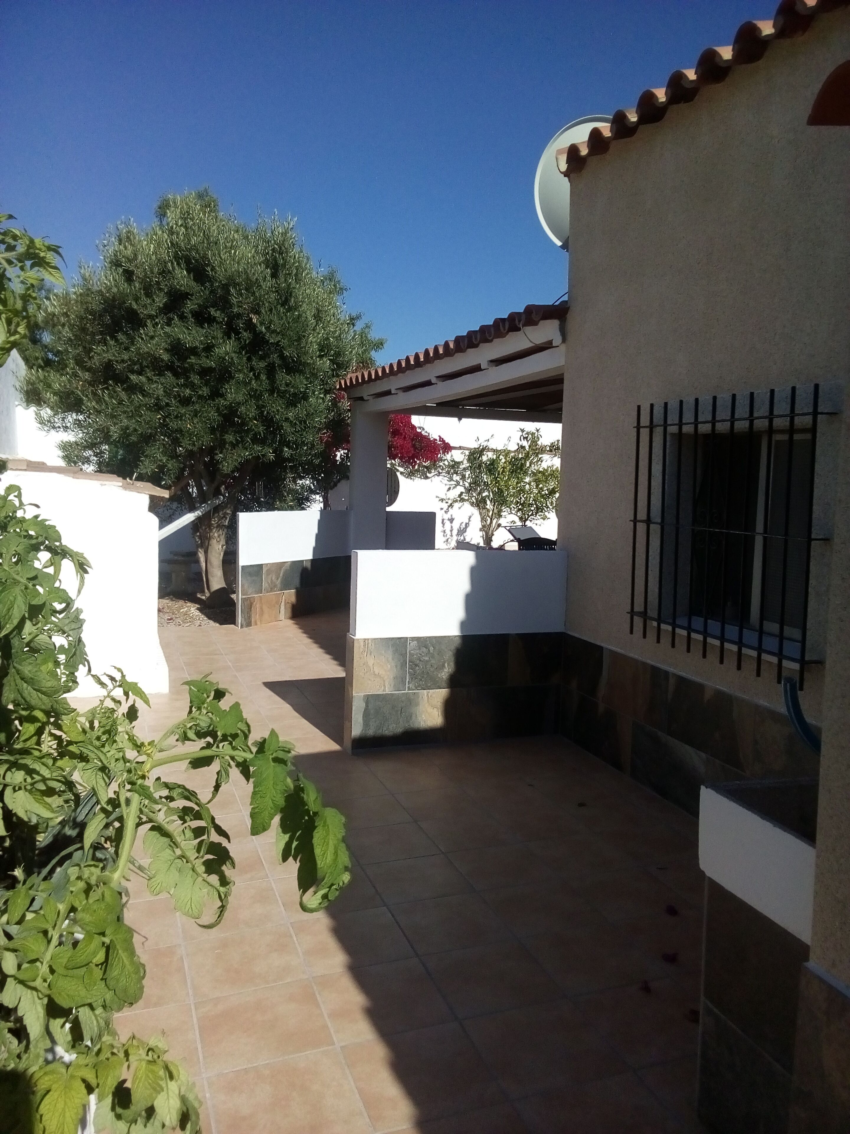 Ein überdachter Patio-Bereich mit Fliesenboden, einer Pergola und einer weißen Wand mit einem Fenster.