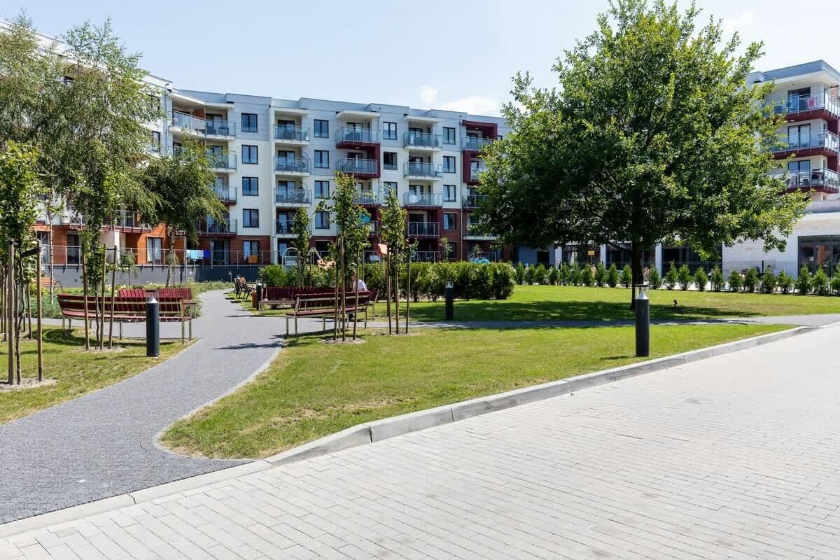 Ein modernes Mehrfamilienhaus mit Balkonen, einem gepflasterten Weg und Bänken in einer angelegten Grünfläche.