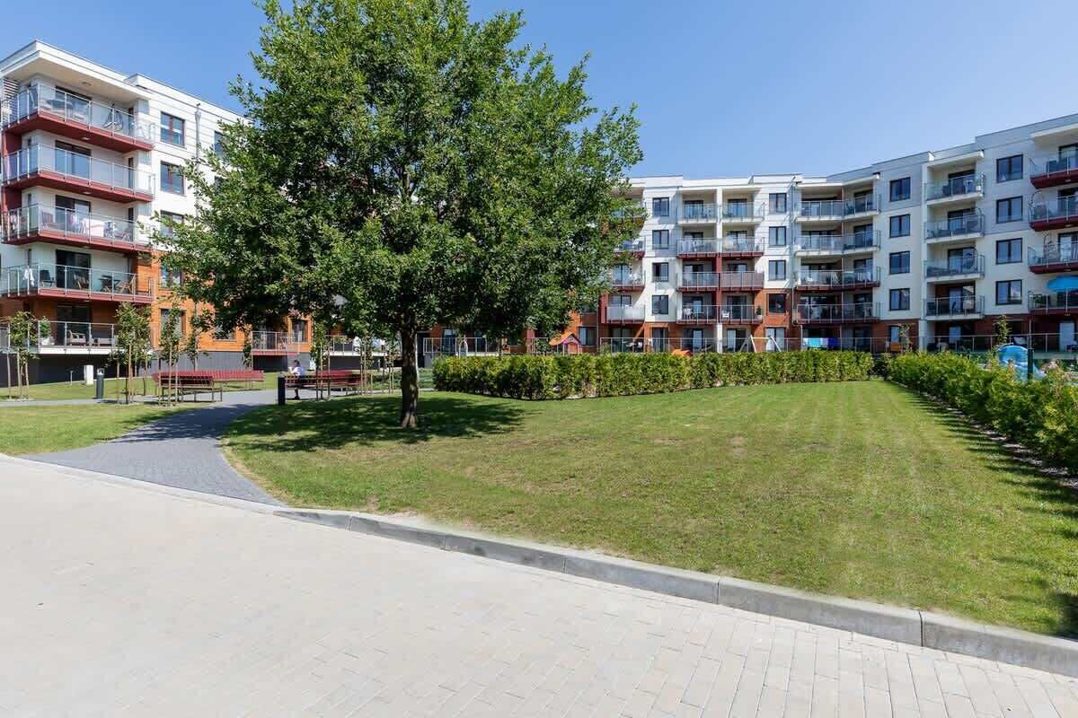 A residential building with multiple balconies, a central lawn, and a paved walkway.
